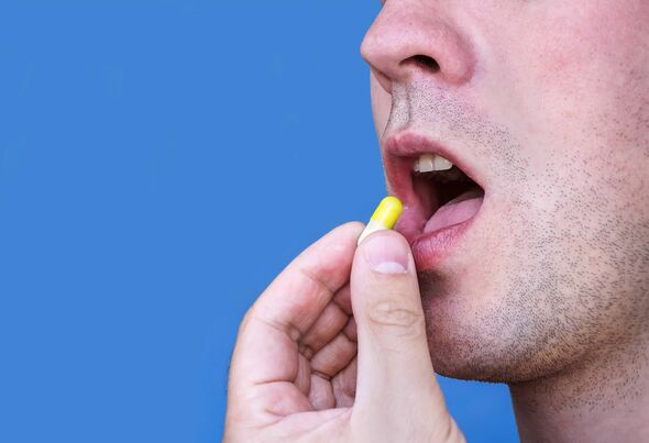 Chàng trai trẻ đặt viên thuốc màu vàng vào miệng, hình ảnh được tách biệt trên nền xanh. Chàng trai nuốt thuốc.