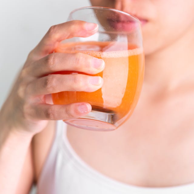Người phụ nữ ăn chay đang uống nước ép rau củ giải độc từ cà rốt tươi. Người phụ nữ đang cầm ly nước ép cà rốt tươi.